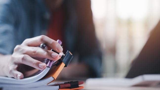 Nahaufnahme einer Person, die konzentriert in ein Notizbuch schreibt, mit einem klaren Blick auf ihre Hand und den Stift. (Link zur Seite Ausschreibungen)